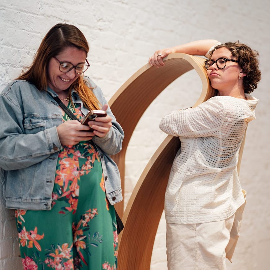 Two adult females closely interacting with a life sized wooden sculpture