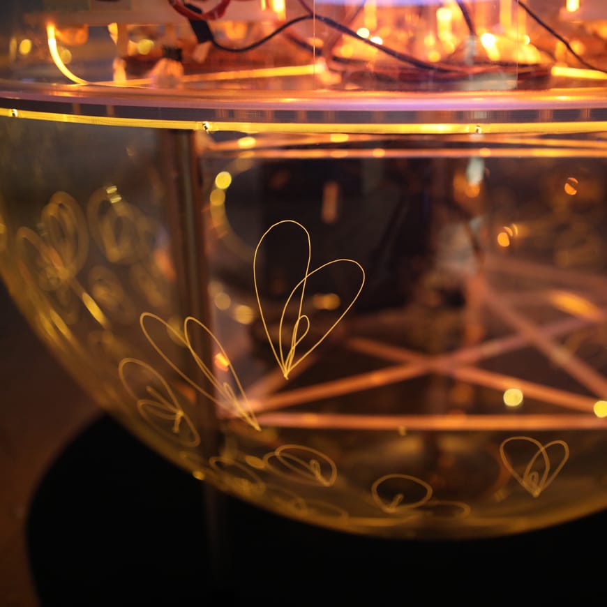 Close-up of transparent sphere containing electronics and LEDs and lit by an internal amber glow