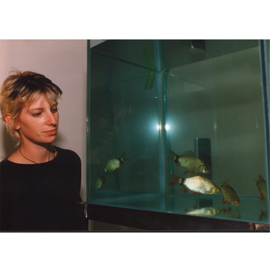 Blonde white female in a black top standing next to tank of fish