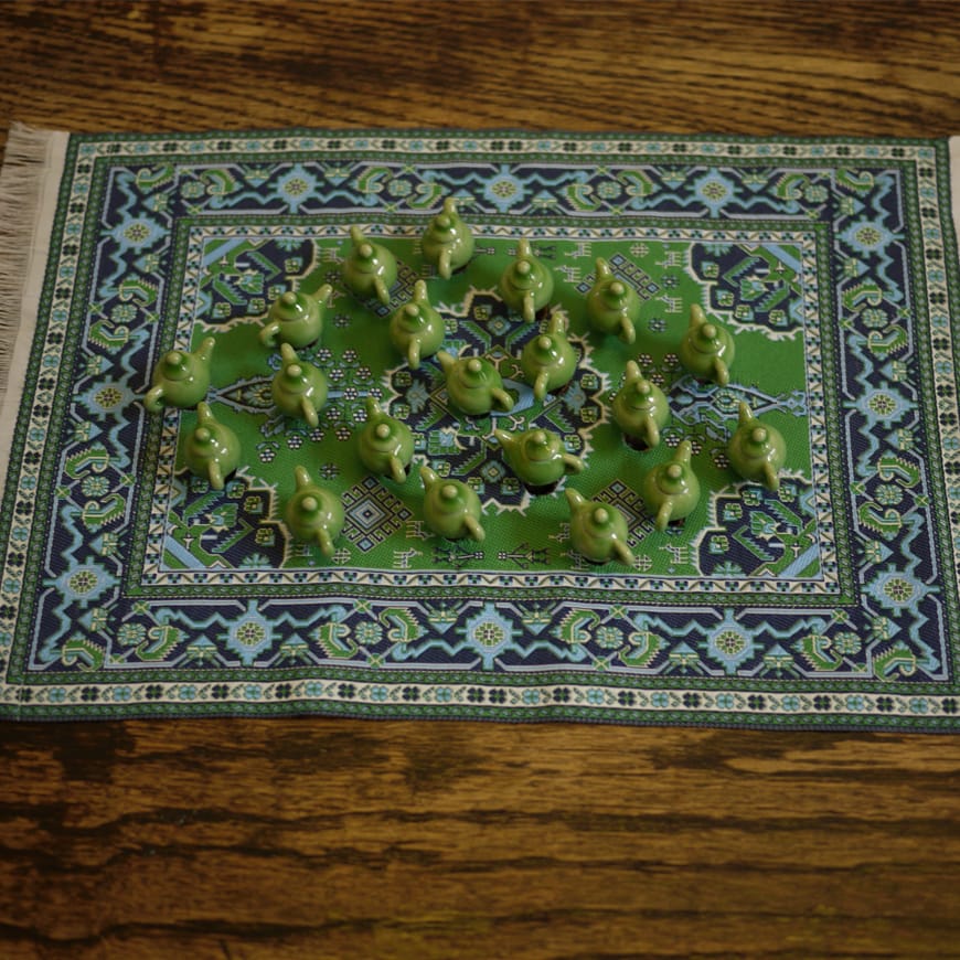 A series of miniature green teapots shown on a small rug