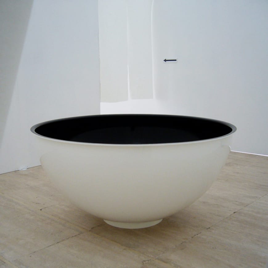 Large white bowl with a black glossy interior, sitting on a wooden floor