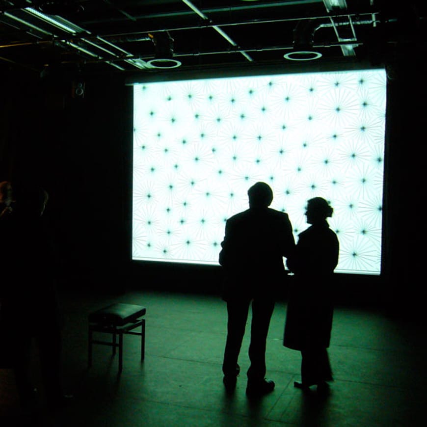 Two standing figures silhouetted in front of a large video projection