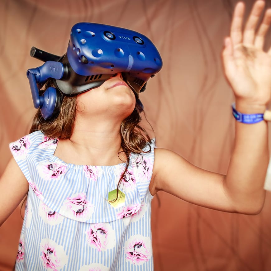 A young person with long hair wearing a VR headset and reaching one hand upwards