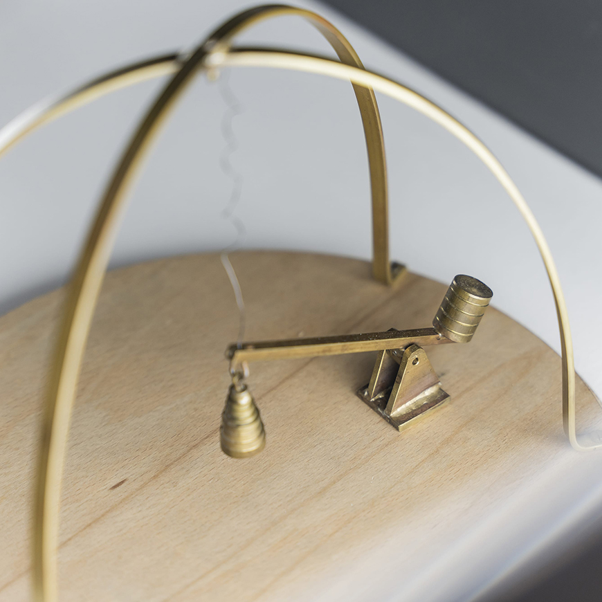 Kinetic sculpture made of a round wooden base with a small brass lever and a brass open cage