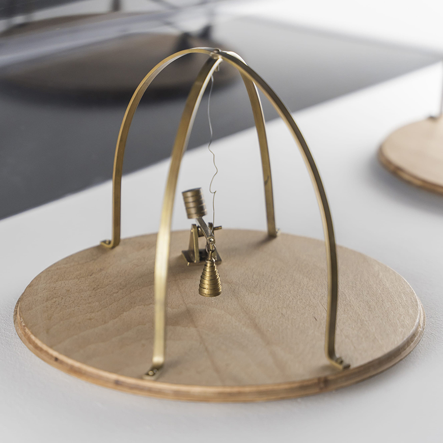 Kinetic sculpture made of a round wooden base with a small brass lever and a brass open cage